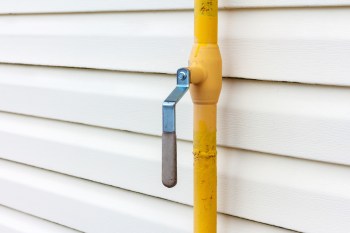 A yellow gas pipe line with a metal handle mounted against white siding.