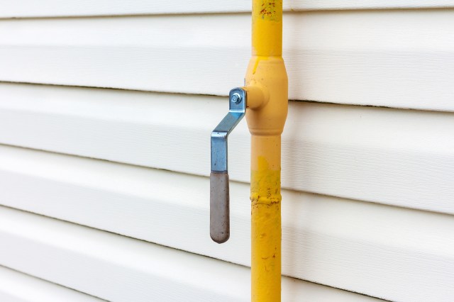A yellow gas pipe line with a metal handle mounted against white siding.