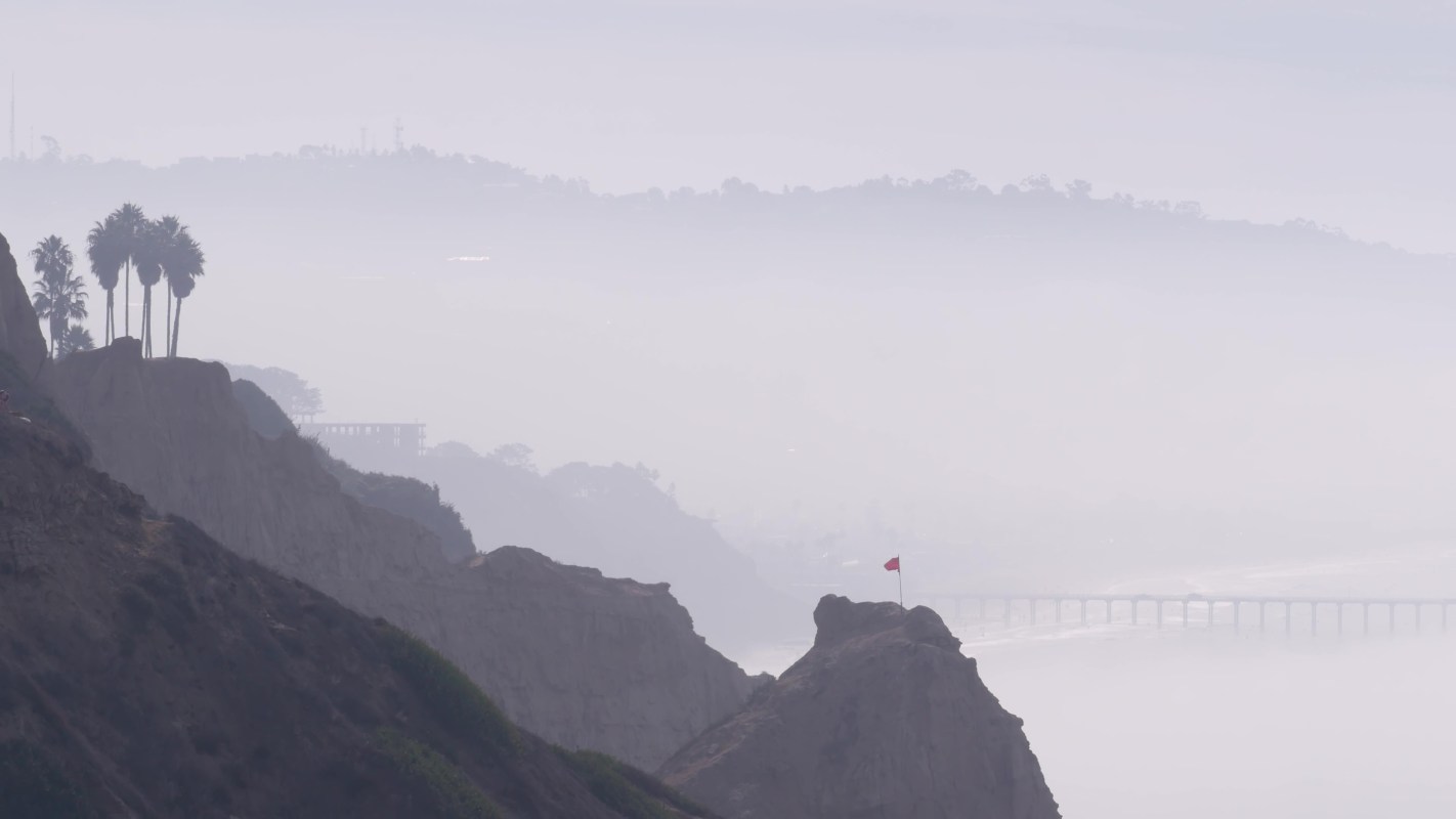 A coastal landscape featuring cliffs and a bridge shrouded in fog.