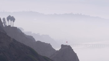 A coastal landscape featuring cliffs and a bridge shrouded in fog.