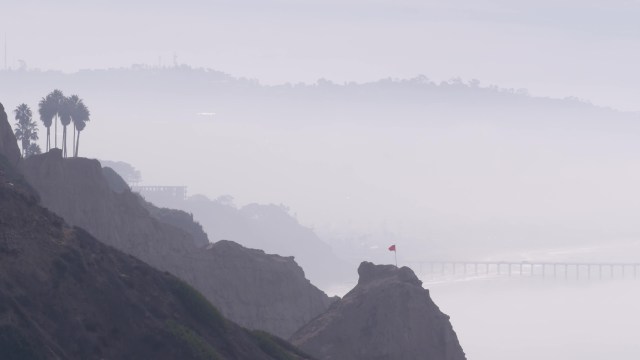 A coastal landscape featuring cliffs and a bridge shrouded in fog.