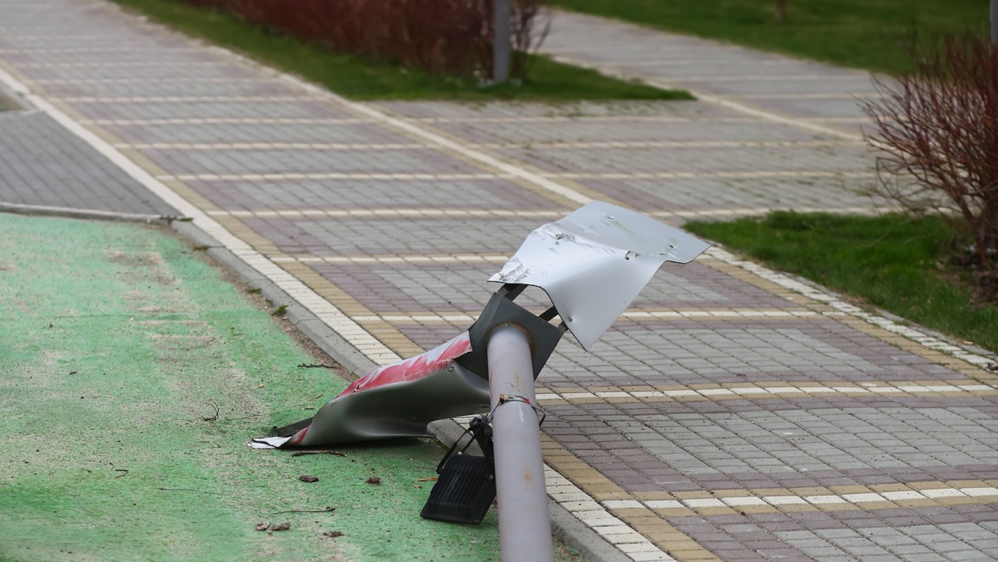 A damaged street sign lying on a sidewalk next to a green path and patterned pavement.