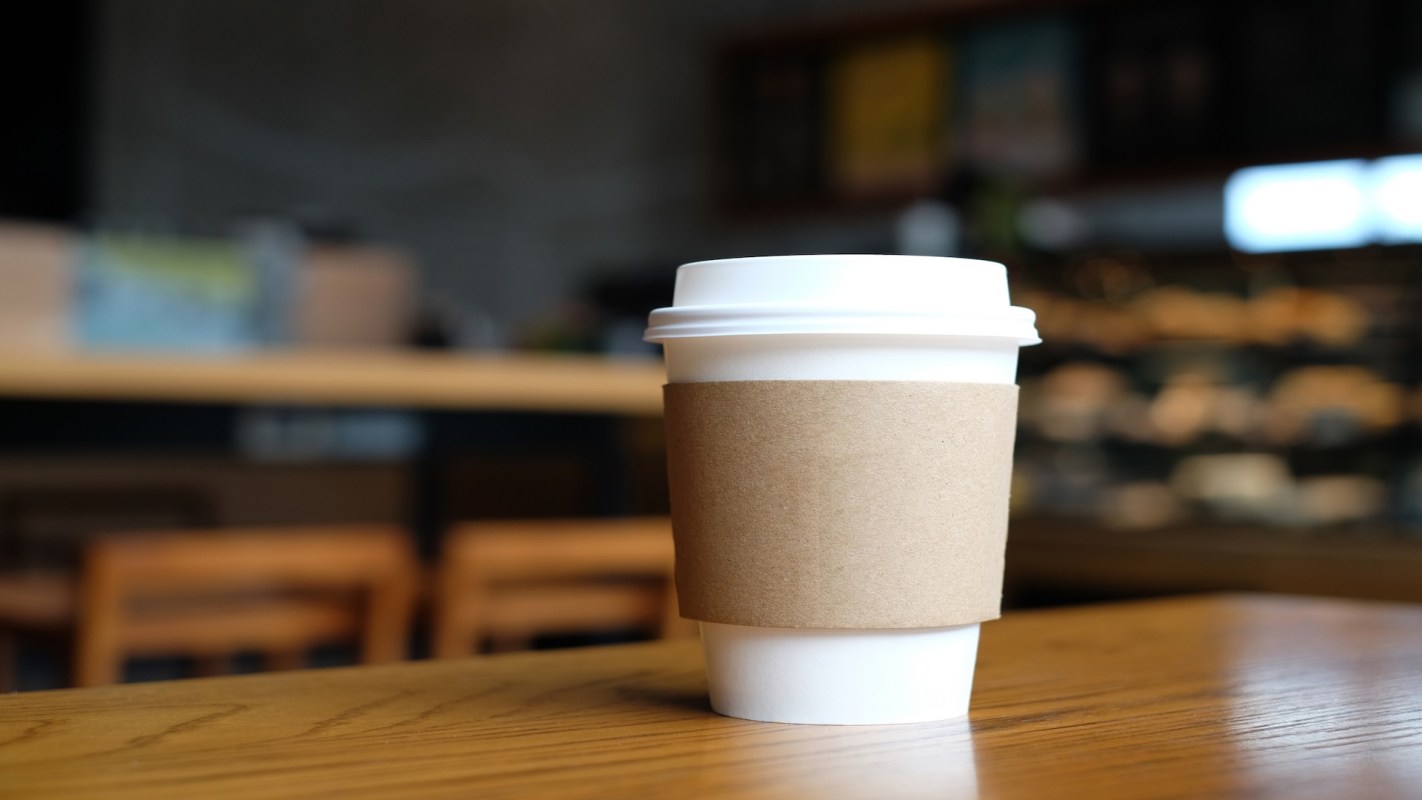 A white coffee cup with a brown sleeve on a wooden table in a café.