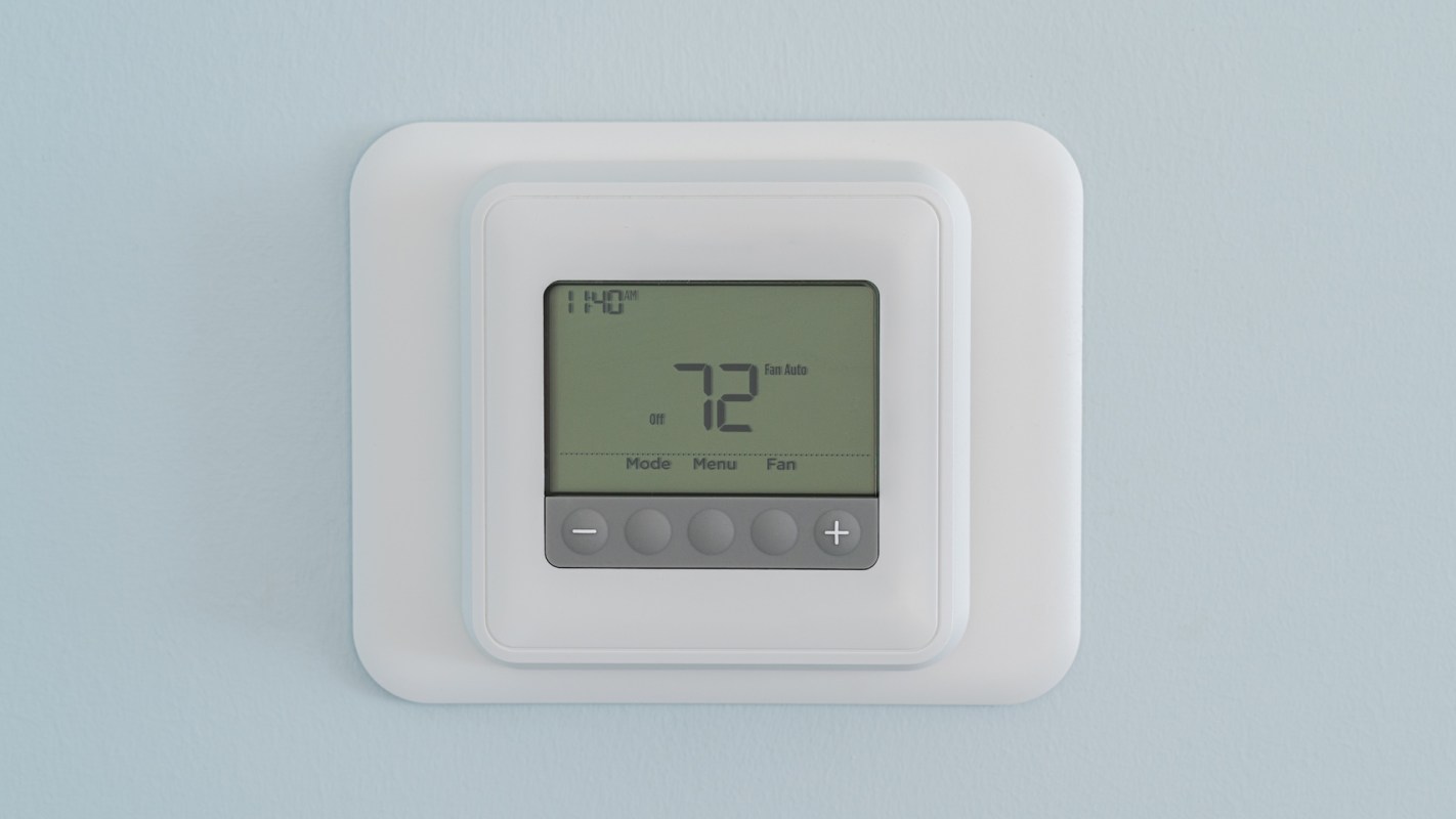 A digital thermostat displaying a temperature setting of 72 degrees on a light blue wall.