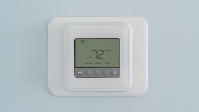 A digital thermostat displaying a temperature setting of 72 degrees on a light blue wall.