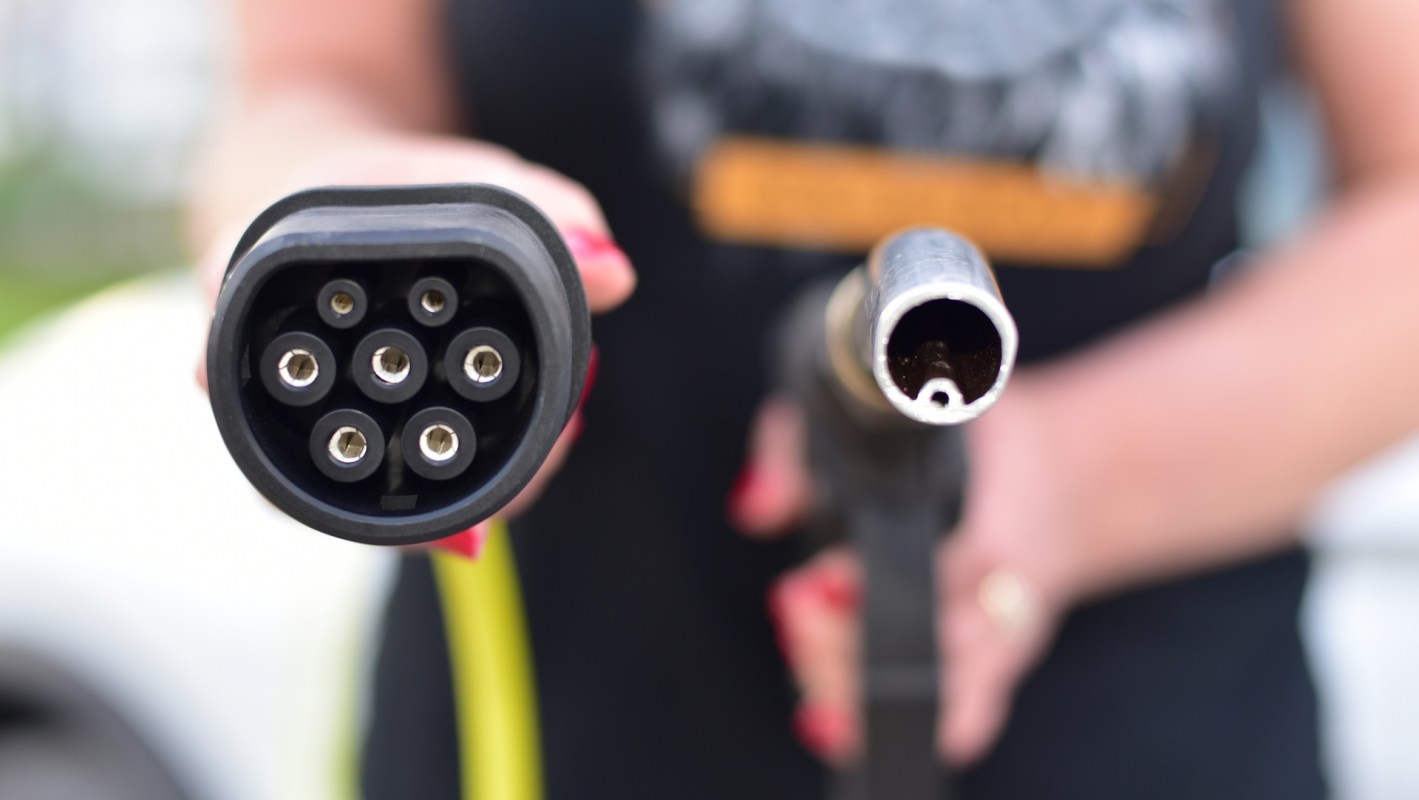 A person holding an EV charger and a gas nozzle.
