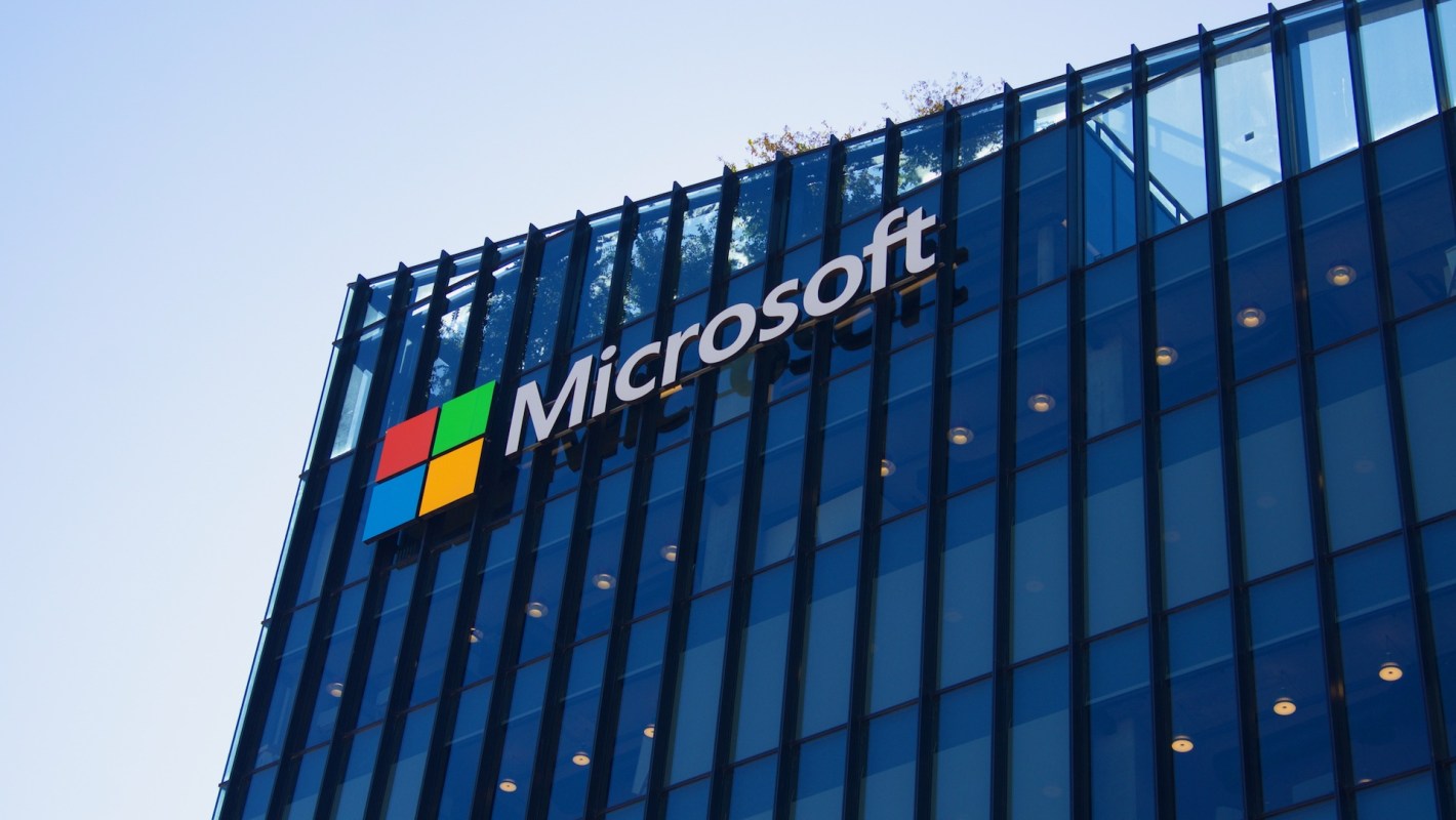 A Microsoft logo on a modern glass building against a clear sky.