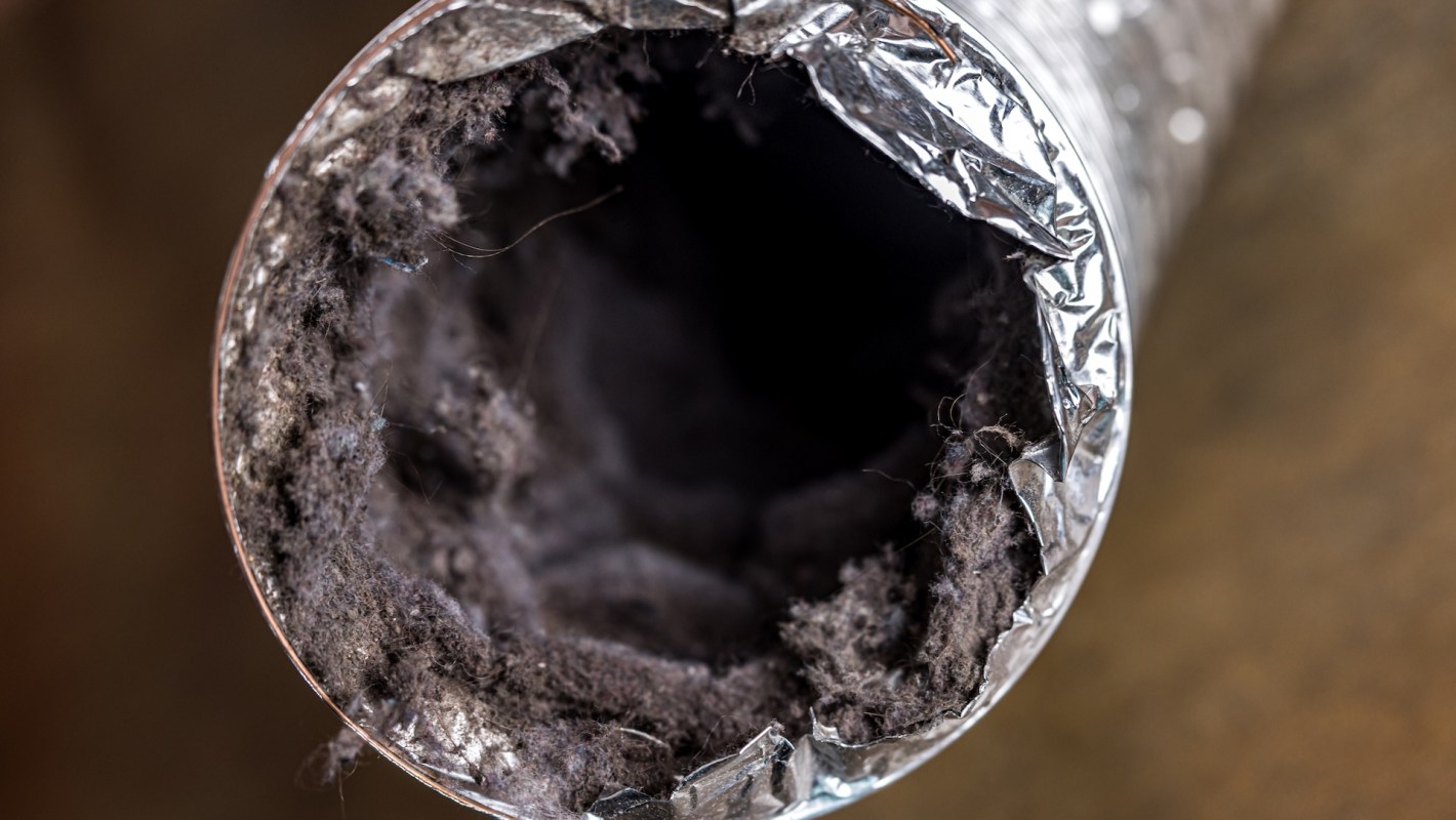 A close-up of the inside of a metallic duct showing accumulated lint and debris.