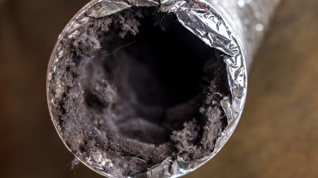 A close-up of the inside of a metallic duct showing accumulated lint and debris.