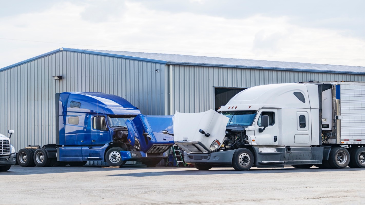 Two semi trucks with raised hoods in front of a warehouse.