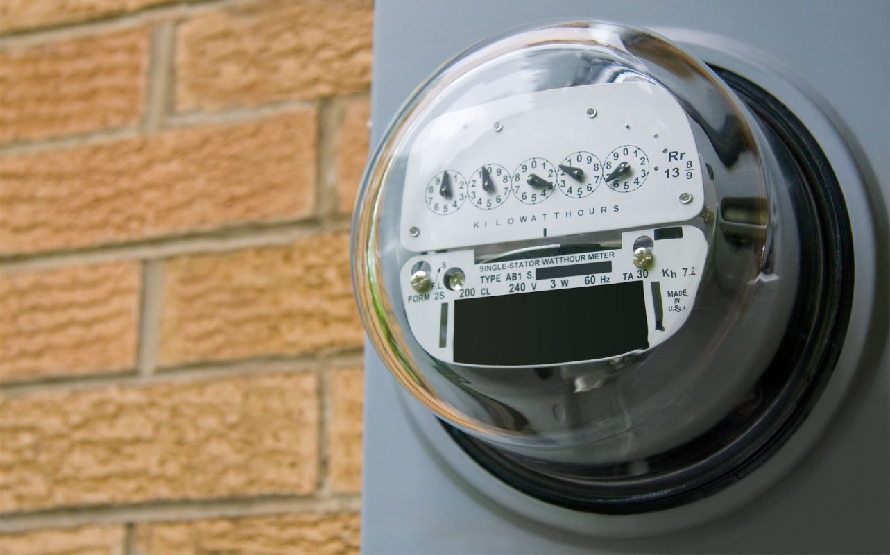 An electric meter mounted on a wall beside brickwork.