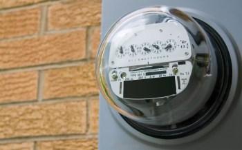 An electric meter mounted on a wall beside brickwork.