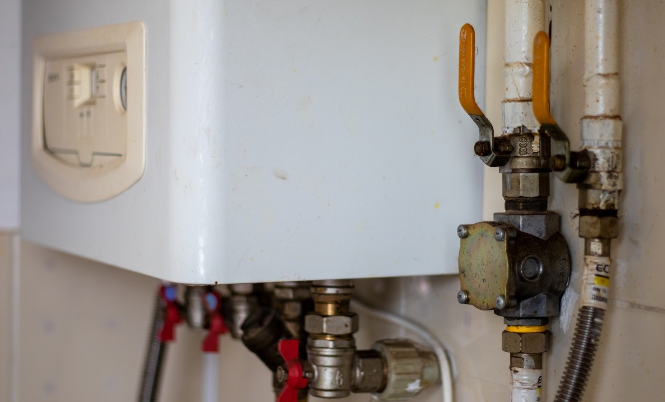 A white heating unit with connected pipes and valves on a wall.