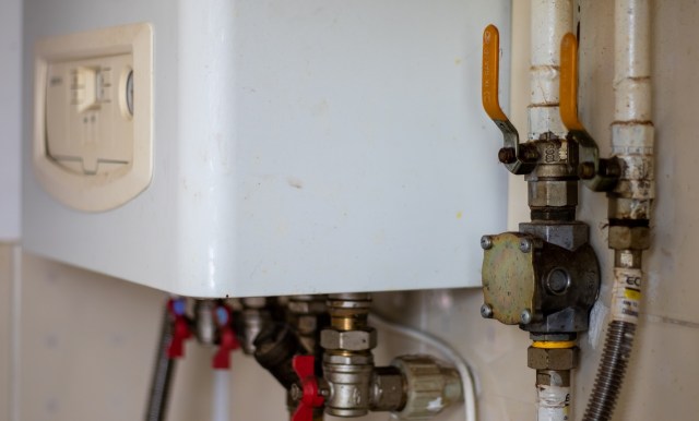 A white heating unit with connected pipes and valves on a wall.