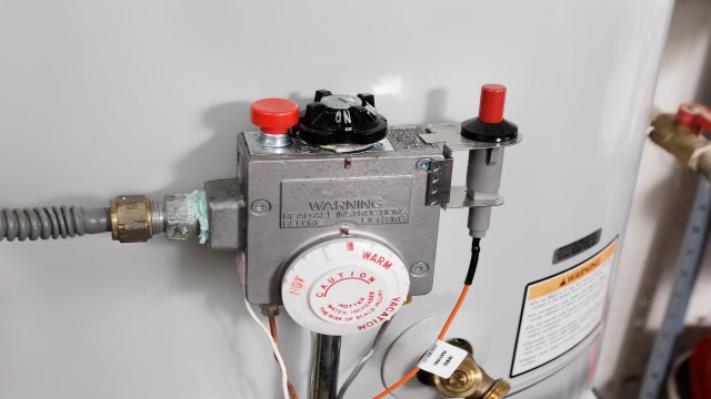 A gas control valve with buttons and a warning label attached to a water heater.