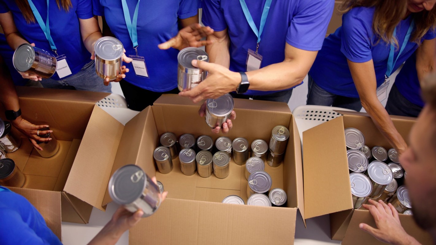 Volunteers sort and package canned goods in cardboard boxes.