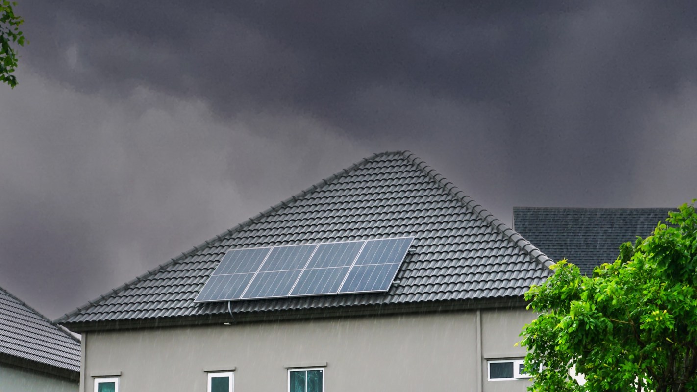 A house with solar panels on the roof under a dark, cloudy sky.