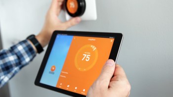 A person adjusts a smart thermostat to 75 degrees using a tablet displaying temperature settings.