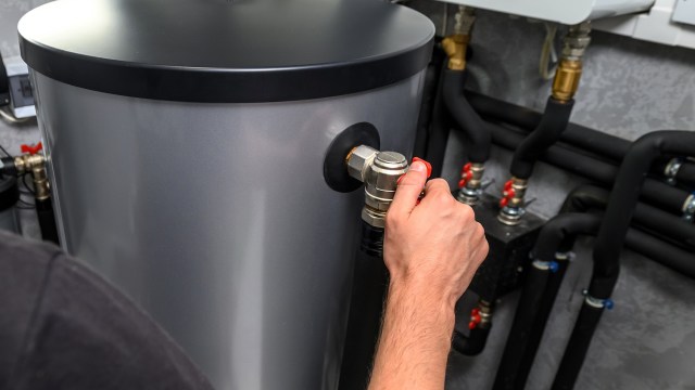 A person operates a valve on a water heater surrounded by pipes and fittings.