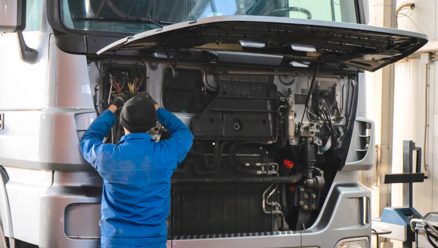 A person works on the engine compartment of a truck.