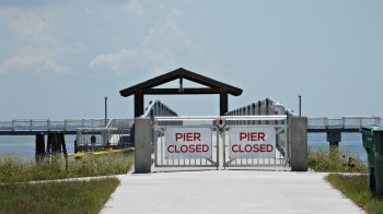 A closed pier entrance with gates displaying "PIER CLOSED" signs and a view of the water in the background.