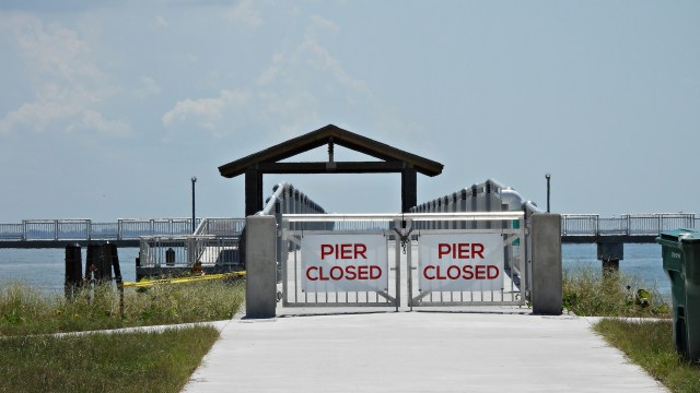 A closed pier entrance with gates displaying "PIER CLOSED" signs and a view of the water in the background.