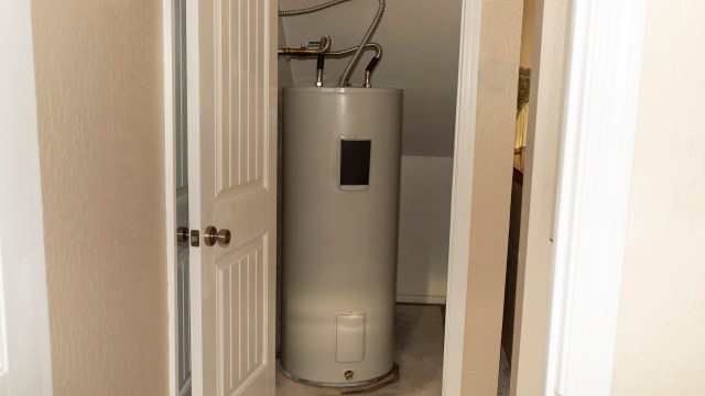 A water heater in a small closet with two doors slightly ajar.