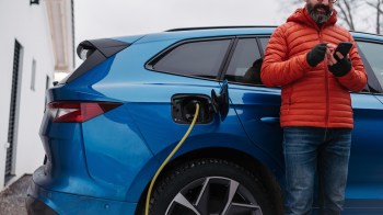 A man stands next to a blue electric vehicle while charging it.