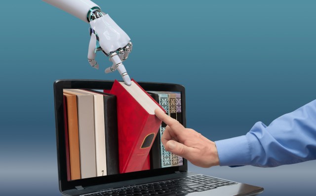 A robotic hand reaches for a book while a human hand points at a laptop displaying books.