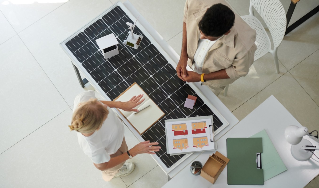 Two people discuss designs at a table featuring solar panels and architectural sketches.