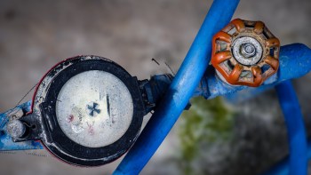A close-up of a water meter and an orange valve on blue pipes.