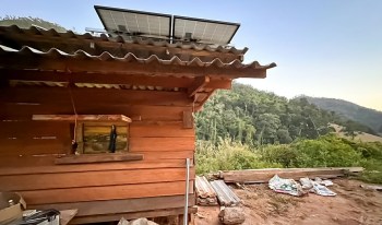A wooden cabin with solar panels on the roof and scattered construction materials nearby.