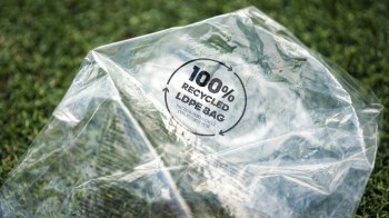 A clear plastic bag labeled "100% recycled LDPE bag" on green grass.