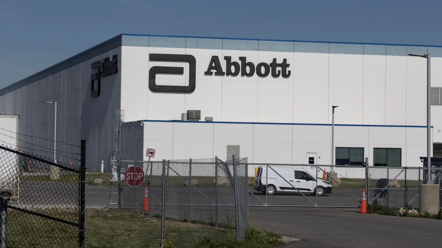 A large industrial building with the "Abbott" logo, surrounded by a fence and parking area.