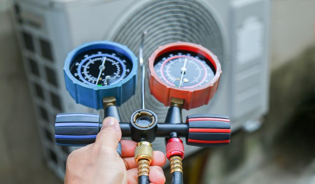 A person holds a set of pressure gauges connected to an air conditioning unit.