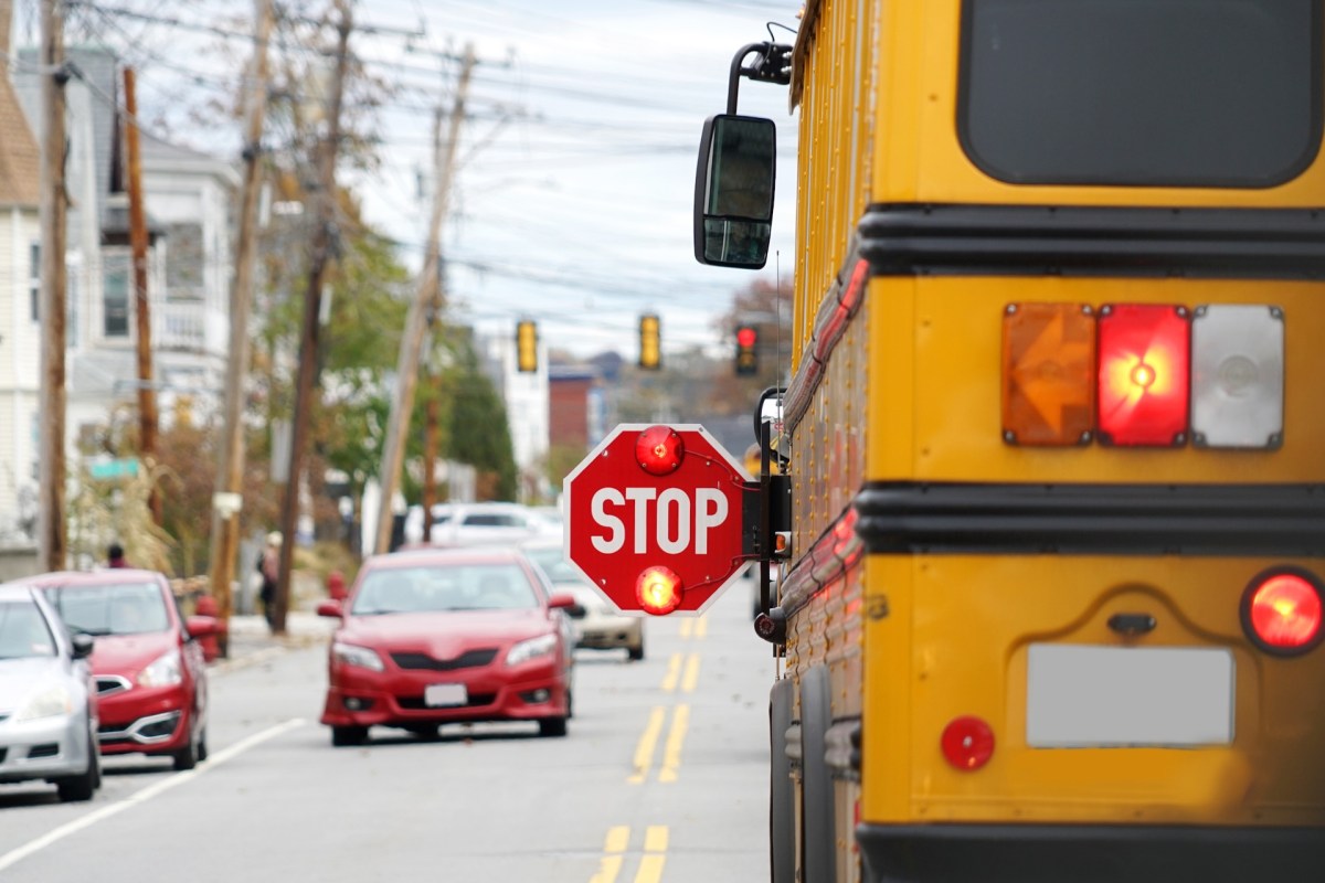 A yellow school bus with a stop sign extended on a city street.