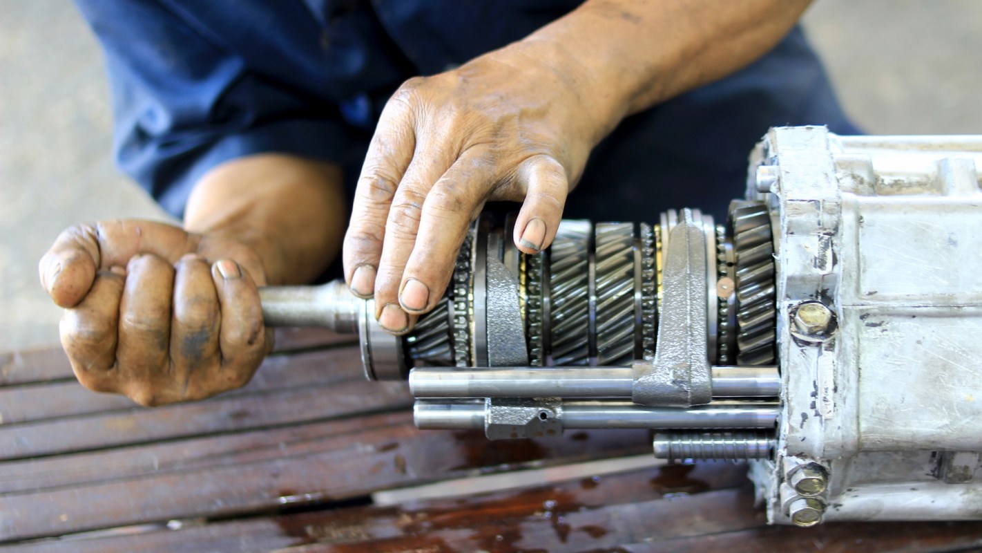 A person working on a disassembled mechanical transmission with dirty hands.