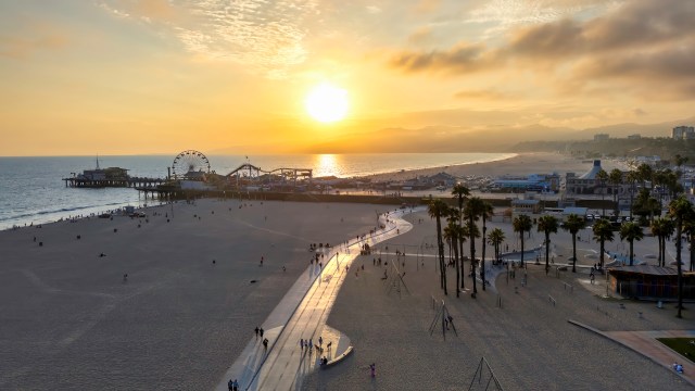 A beach scene in Santa Monica, California, at sunset with a pier, amusement rides, and people strolling along the shoreline.