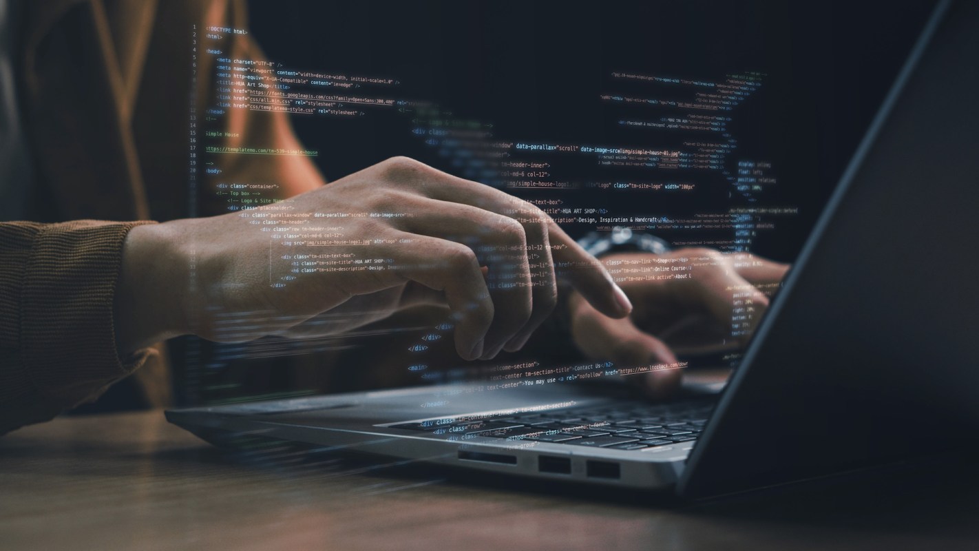 A person types on a laptop with code displayed on the screen.