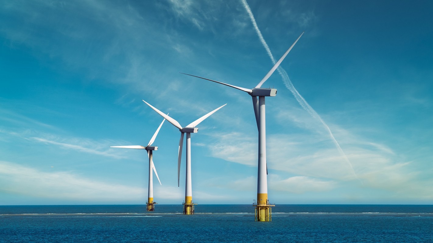 Three wind turbines stand in the ocean against a clear blue sky.