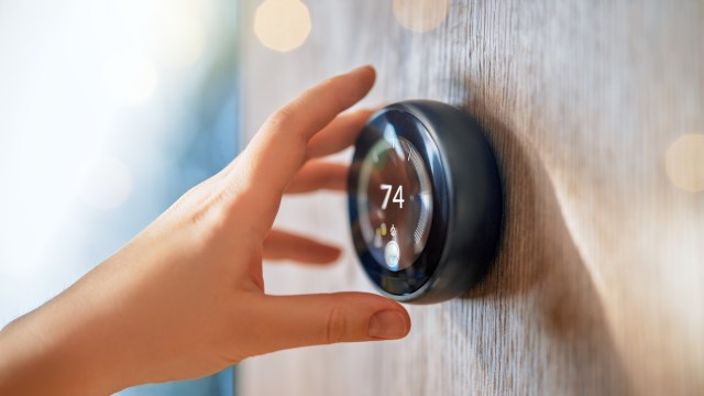A hand adjusts a thermostat displaying a temperature of 74 degrees.