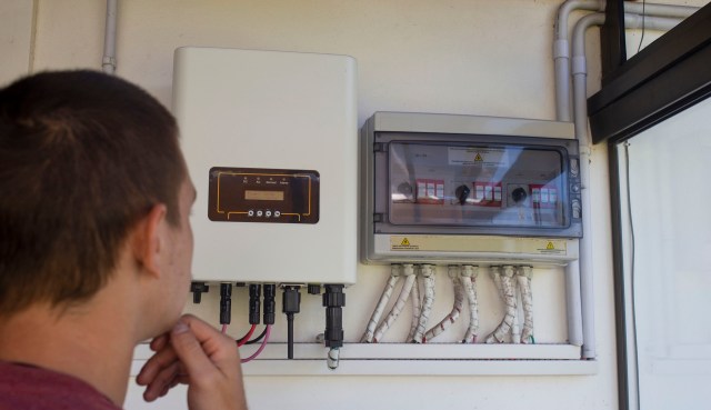 A person looks at electrical control panels for solar energy mounted on a wall.