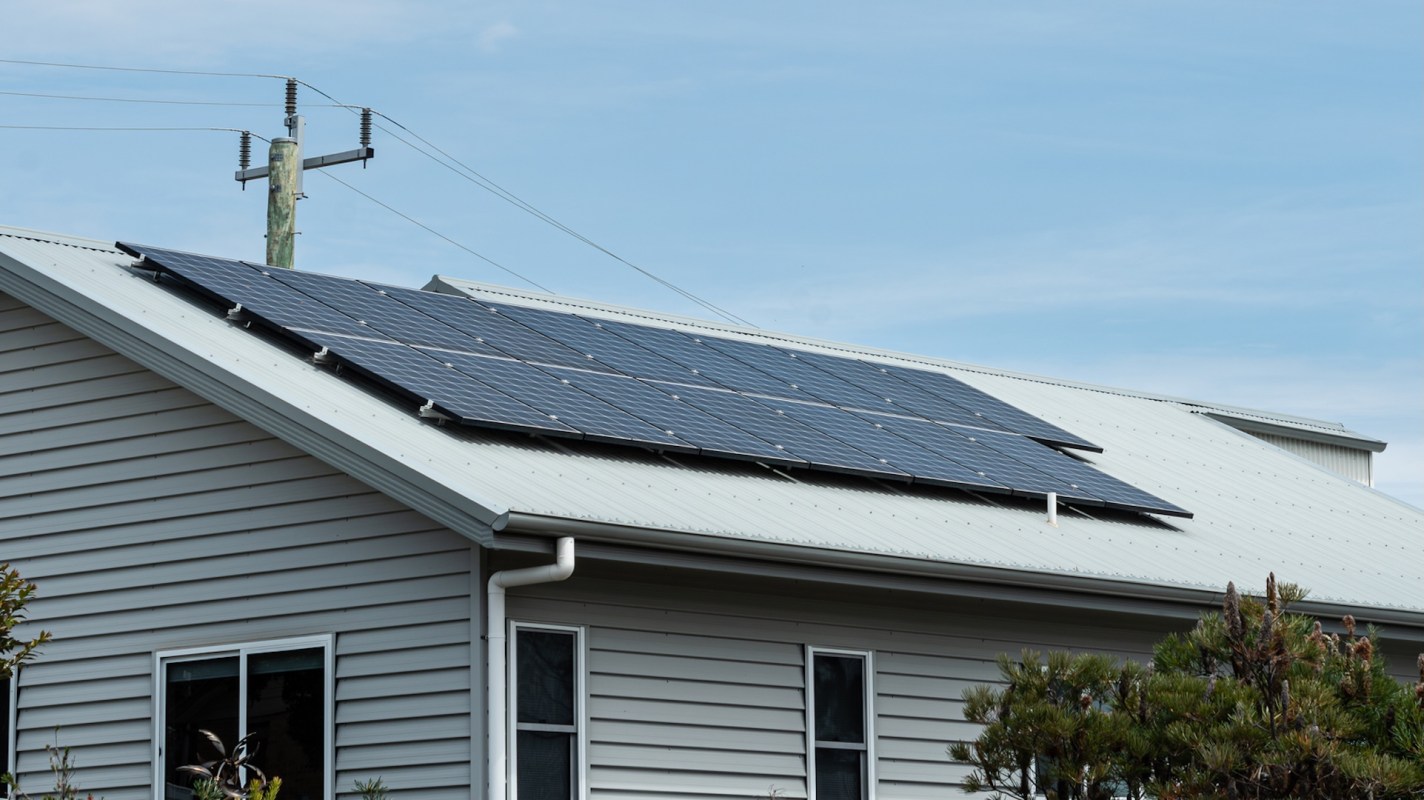 Solar panels installed on a sloped metal roof of a house, with power lines in the background.