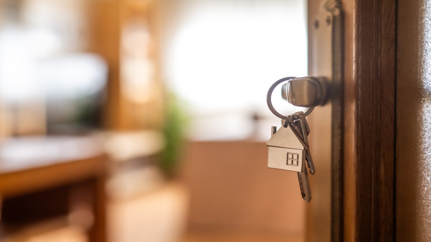 A key with a house-shaped keychain is hanging from a door lock.