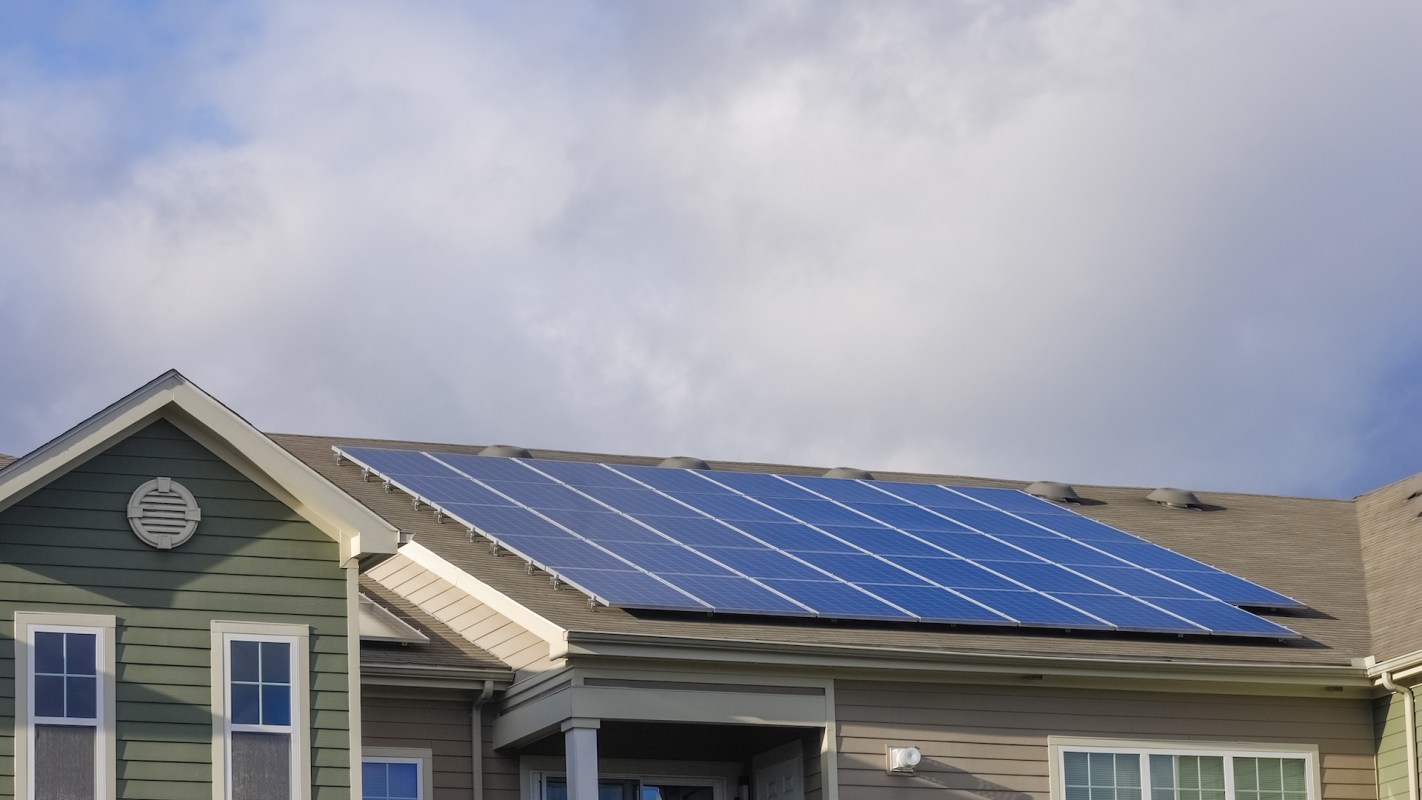 A house with solar panels installed on the roof under a cloudy sky.