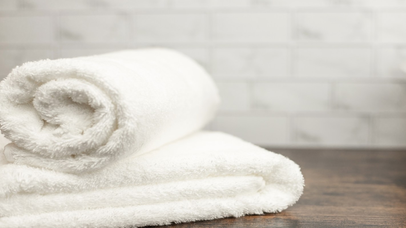 Two neatly rolled white towels placed on a wooden surface with a textured background.