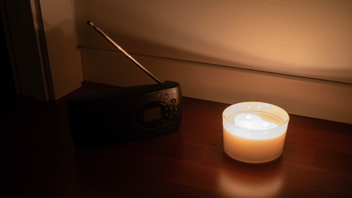 A radio next to a glowing candle on a wooden floor.