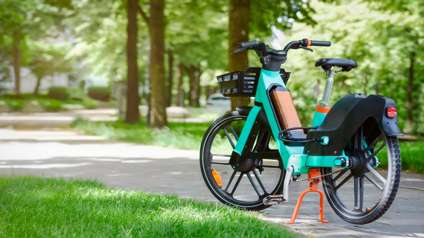 A blue and black bicycle with a basket parked on a pathway in a green park.