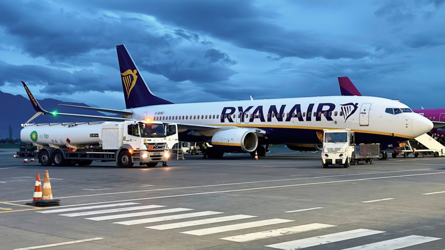 A Ryanair airplane on the tarmac with refueling trucks nearby and cloudy skies in the background.