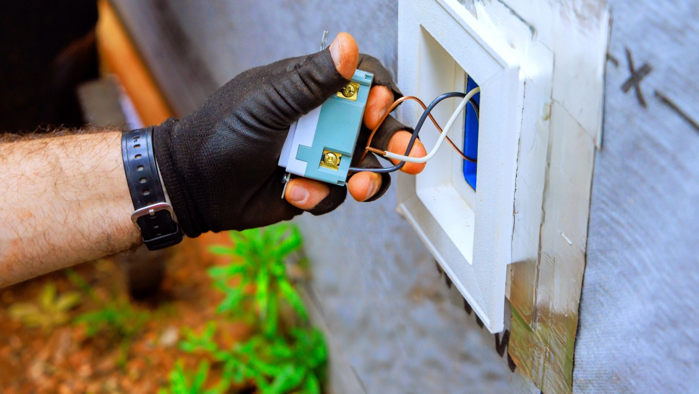 A person holding electrical wiring from an outlet.